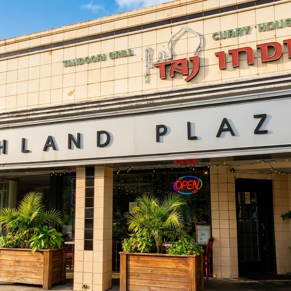 Taj India Curry House restaurant entrance at Highland Plaza, with illuminated open sign and tropical plants in wooden planters.